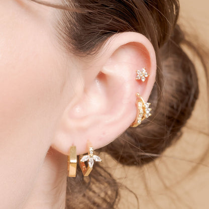 Gold Hex Huggie Earring on left ear surrounded by other pieces of Jewellery